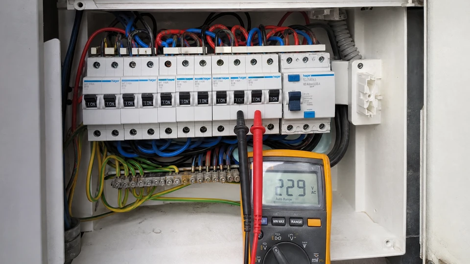 Électricien professionnel travaillant sur installation électrique résidentielle, manipulant multimètre et câblage dans boîtier mural
